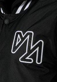Veste noire avec un logo brodé texturé en blanc. Équipée d'une fermeture à boutons et d'un col rayé contrastant. Texture de tissu lisse.