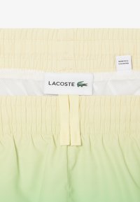 Costumi da bagno giallo-verde chiaro caratterizzati da un elastico in vita, etichetta con logo Lacoste e un design a gradiente morbido.