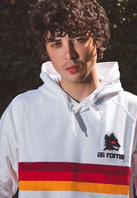 Witte hoodie met rode en gele horizontale strepen, voorzien van een zwart wolf logo en de tekst "as roma" op de borst. Zachte stoftextuur.