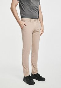 Beżowe spodnie wąskie z zapięciem na guziki, z kieszeniami po bokach. Połączone z dopasowanym szarym T-shirtem i czarnymi trampkami.