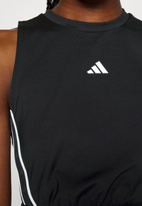 Gros plan d'une personne portant un haut sans manches noir Adidas avec un logo blanc et des bandes blanches sur le côté.
