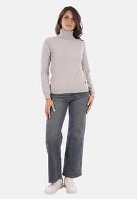 Maglione grigio chiaro a collo alto con una texture morbida, indossato con jeans a gamba larga blu e sneakers bianche. Dettagli sottili all'orlo del maglione.