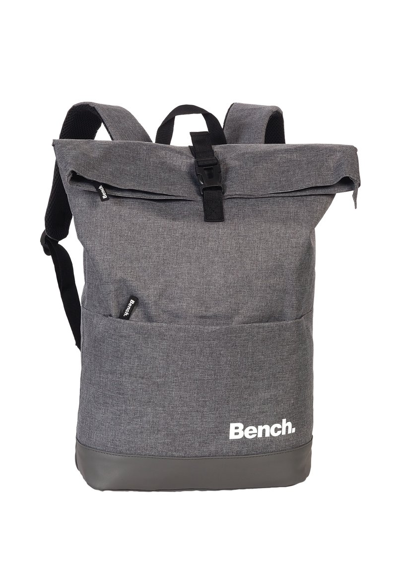 Sac à dos en tissu gris avec un design à rabat, présentant des accents noirs, des bretelles ajustables, des poches extérieures et un logo sur le devant.