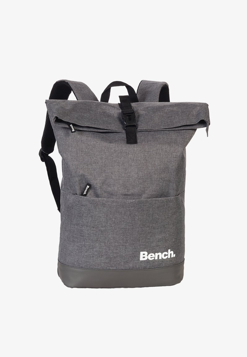 Sac à dos en tissu gris avec un design à rabat, présentant des accents noirs, des bretelles ajustables, des poches extérieures et un logo sur le devant.