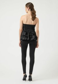 Czarny top bez ramiączek z marszczoną górą i falbaniastą spódnicą z tkaninowymi różami, zestawiony z czarnymi legginsami i butami na obcasie.