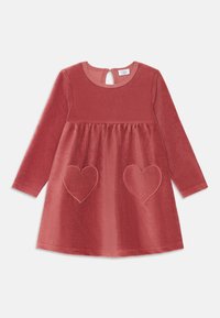 Vestido de pana rojo con mangas largas, escote redondo y espalda con abertura en forma de llave. Presenta dos bolsillos en forma de corazón con detalles de costura.