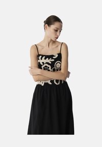 Zwarte jurk met een haakwerk bodice en witte bloemenpatronen, verstelbare spaghettibandjes en een geplooide taille.