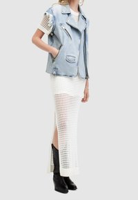 Jeansmotorcykeljacka med dragkedjor, ljusblå. Vit stickad maxiklänning med öppen väv och sidoklyfta. Svarta klackstövlar.