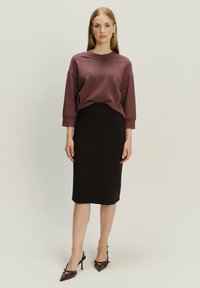 Pulover u dubokoj ružičastoj boji, opuštenog kroja s spuštenim ramenima. Crna midi suknja s prugastim siluetom, upotpunjena cipelama s špicastim nosom.