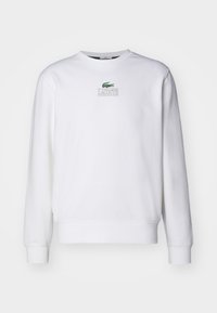 Biała bluza z bawełnianej mieszanki, z prążkowanymi mankietami i zakończeniem, oraz małym zielonym logo Lacoste wyhaftowanym na piersi.