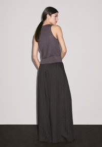Haut sans manches violet avec une finition texturée associé à un pantalon large à rayures noires, présentant une silhouette décontractée et une taille élastique.