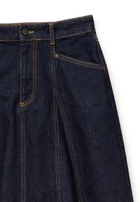 Donkerblauwe denimrok met gele stiksels, knoopsluiting aan de voorkant, riemlussen en een schuine voorkantzak op een witte achtergrond.