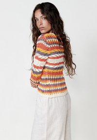 Suéter de punto con rayas multicolores en naranja, amarillo y gris. El diseño incluye una textura de encaje y un fondo ajustado con ribete.