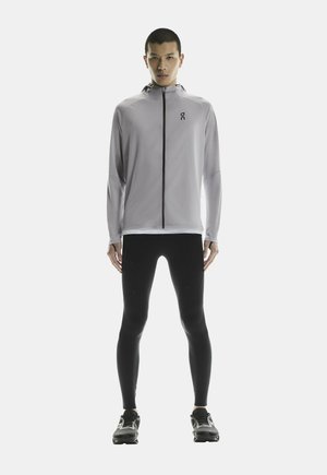 Light gray athletic jacket with a high collar and full zipper, paired with black leggings and running shoes, featuring a sleek design.