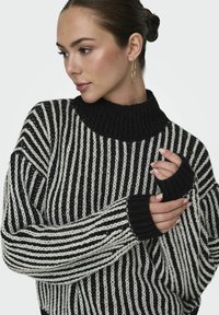 Črno-bela prugasta pletena jopica z rebrastim turtleneck ovratnikom, ki ima luknje za palce in sproščen kroj, z teksturirano tkanino.