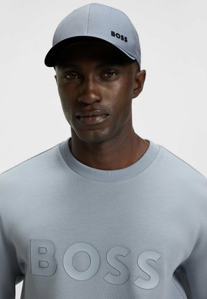 Gray cap with black "BOSS" logo, paired with a light gray sweatshirt featuring a large embossed "BOSS" text. Smooth fabric texture.