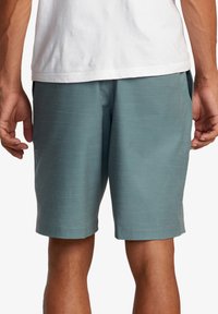 Shorts teal fabriqués en tissu léger, présentant une texture subtile. L'ourlet arrive au-dessus du genou, avec des poches latérales et une taille élastique.