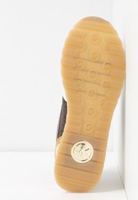 Semelle de basket en caoutchouc avec une surface beige texturée et un accent de logo circulaire. Comprend une tige en tissu foncé et des accents en cuir marron.