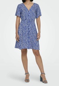 Niebieska sukienka w kwiatowy wzór z dekoltem w serek, krótkimi rękawami, zwężoną talią i rozkloszowanym dołem; zestawiona z niebieskimi sandałami na obcasie.