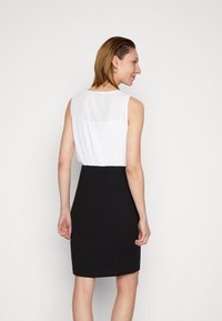 Vestido preto com uma parte superior branca, sem mangas, e uma cintura franzida. Tecido suave; design até ao joelho com uma silhueta ajustada.