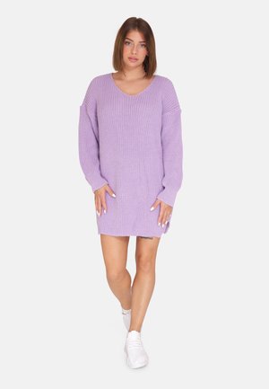 Vestido de punto oversized en color lila con escote en V, mangas largas, aberturas laterales y tejido texturizado, combinado con zapatillas blancas.