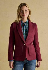 Burgundi värvi kohandatud bleiser tekstureeritud kangast, millel on kaks esi-taskut, ühe nupuga kinnitamine, seljas sinise ja rohelise mustriga särk.