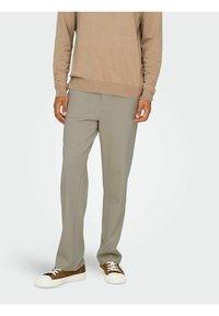 Lys grå strækbukser med lige snit, der har en glat overflade og minimal detaljer. Kombineret med lavtop brune sneakers.