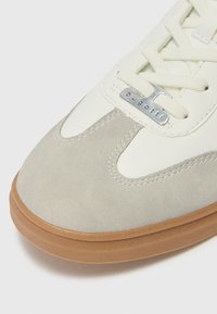 Light gray suede sneaker with a cream leather upper, flat laces, and a rubber tan sole; features a silver "bugatti" logo tag on the side.