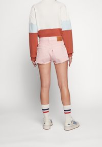 Ljust rosa denimshorts med fransad fåll, tillsammans med en färgblockerad sweatshirt i vitt, rost och blått, samt vita sneakers med blå ränder.