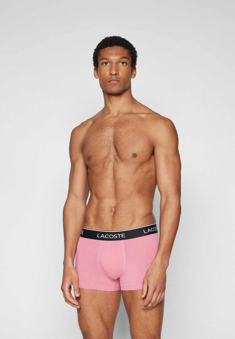 Boxer shorts en coton rose avec une ceinture logo Lacoste noire, présentant un design ajusté et une texture lisse.