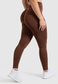 Bruine high-waisted leggings van rekbaar materiaal, met een gladde textuur, een aansluitende silhouette en een subtiele logodetail nabij de tailleband.