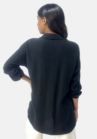 Camicia nera in cotone con una finitura testurizzata e stropicciata, maniche lunghe e una vestibilità rilassata, con orlo e colletto leggermente curvati.