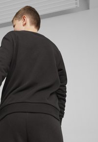 Czarna bluza z miękkiego materiału, z ściągaczami przy mankietach i dolnym wykończeniu. Widok z tyłu pokazuje luźny krój, minimalne szwy i gładką teksturę.