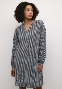 Vestito a righe bianche e nere, con scollatura a V, maniche lunghe e spacchi laterali. Realizzato in tessuto leggero con un design geometrico.