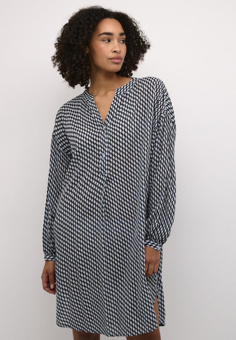 Vestito a righe bianche e nere, con scollatura a V, maniche lunghe e spacchi laterali. Realizzato in tessuto leggero con un design geometrico.