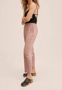 Jasnoróżowe, zwężane spodnie z elastycznym pasem; zestawione z czarnymi klapami z drewnianym obcasem i srebrnymi ćwiekami.