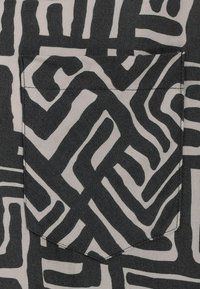 Schwarzer und weißer Stoff mit auffälligen, abstrakten Linien. Verfügt über eine aufgesetzte Tasche oben, eine glatte Textur und ein scharfes geometrisches Design.