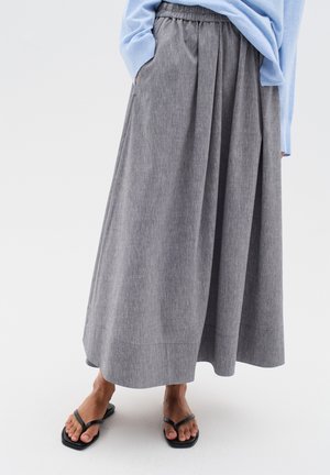 Grå, midi-længde nederdel med en tekstureret stof, plisseringer og en elastisk talje. Bæres med sorte flip-flops, der komplementerer den afslappede stil.