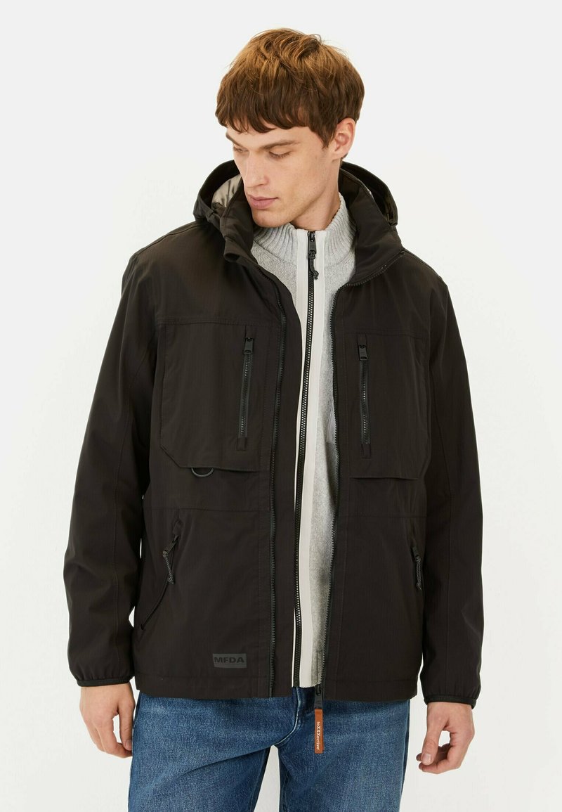 Veste noire imperméable avec capuche, fermeture éclair frontale, plusieurs poches zippées, tissu texturé et accents de fermeture éclair contrastants.