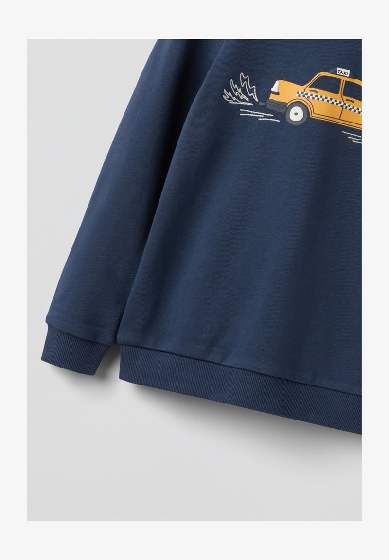 Laivansinis villapaita, joka on valmistettu puuvillasta, jossa on graafinen keltainen taksi, ribbadut hihansuut ja helma. Sujuva tekstuuri ja rento muotoilu.