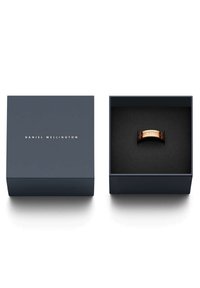 Kuparirengas, jossa on kaiverrettu teksti, esitetty tummansinisessä laatikossa, jossa on kultainen logo. Laatikon sisäosa on pehmeää mustaa materiaalia.