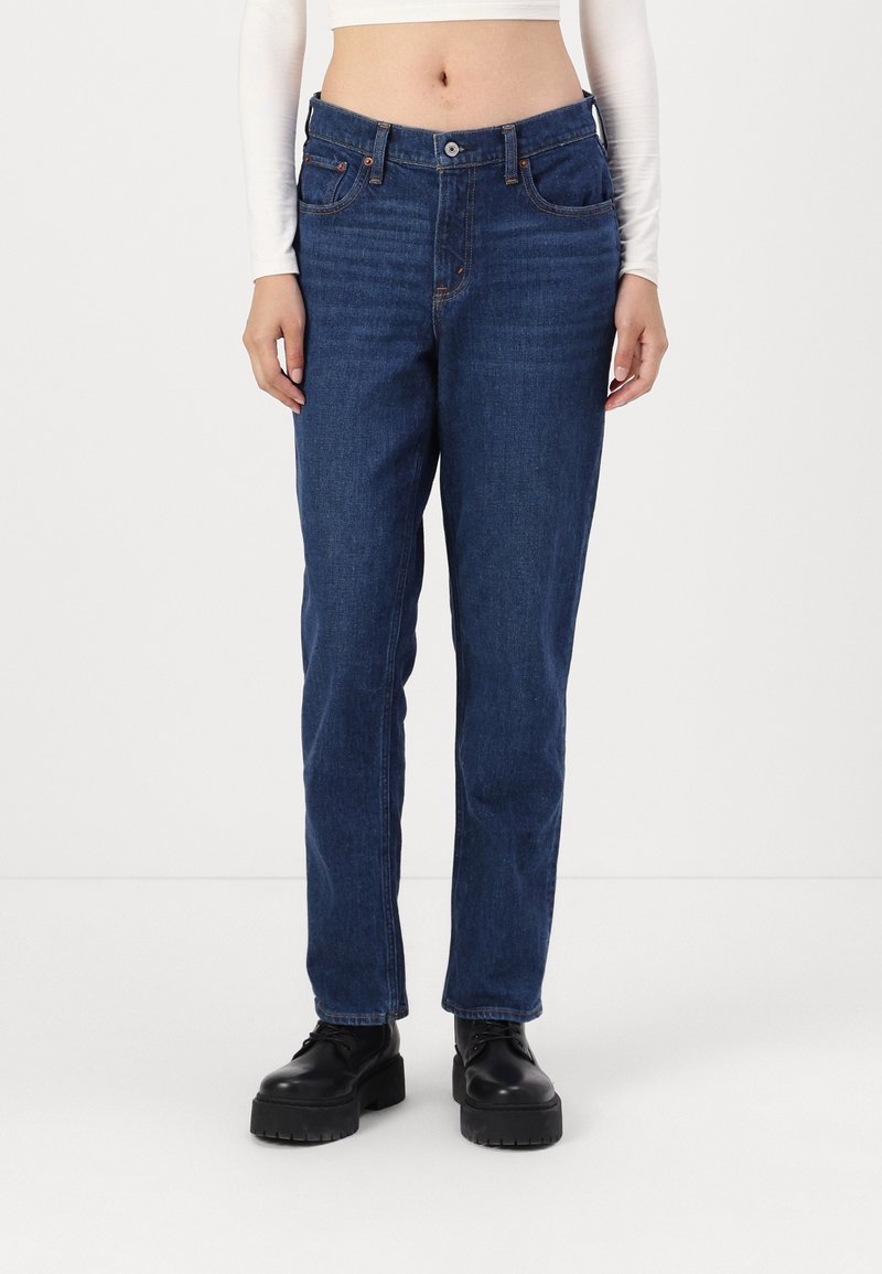 Donkerblauwe denim jeans met een rechte snit, voorzien van voorkruiszakken, riemlussen en een enkele knoopgulp. Gecombineerd met zwarte platformlaarzen.