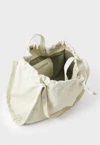 Kremfarget totebag laget av mykt materiale, med snøringåpning, to håndtak og en innvendig glidelommer.