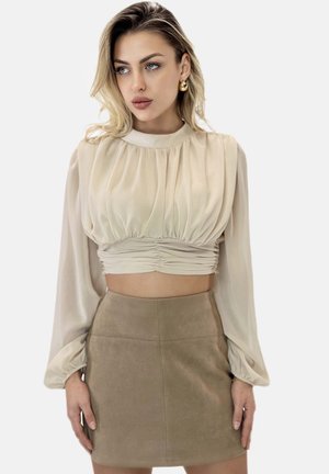 Hellbeige, kurz geschnittene Bluse mit gefaltetem Design, hohem Kragen und langen, gerafften Ärmeln. Kombiniert mit einem taillierten, strukturierten Minirock aus braunem Wildleder.