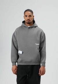 Grijze capuchontrui met een losse pasvorm, voorzien van een voorkantzak en een wit logo. Soepele textuur, geribbelde manchetten en zoom.