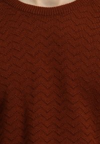 Sweter w kolorze rdzawego, z dzianiny, z teksturowanym wzorem w zygzaki, z klasycznym okrągłym dekoltem i prążkowanymi detalami przy kołnierzu.