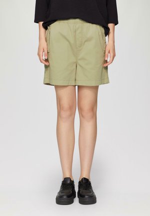 Khaki shorts met een elastische tailleband, zijzakken en een rechte snit, gecombineerd met zwarte sneakers. De stof lijkt zacht en duurzaam.