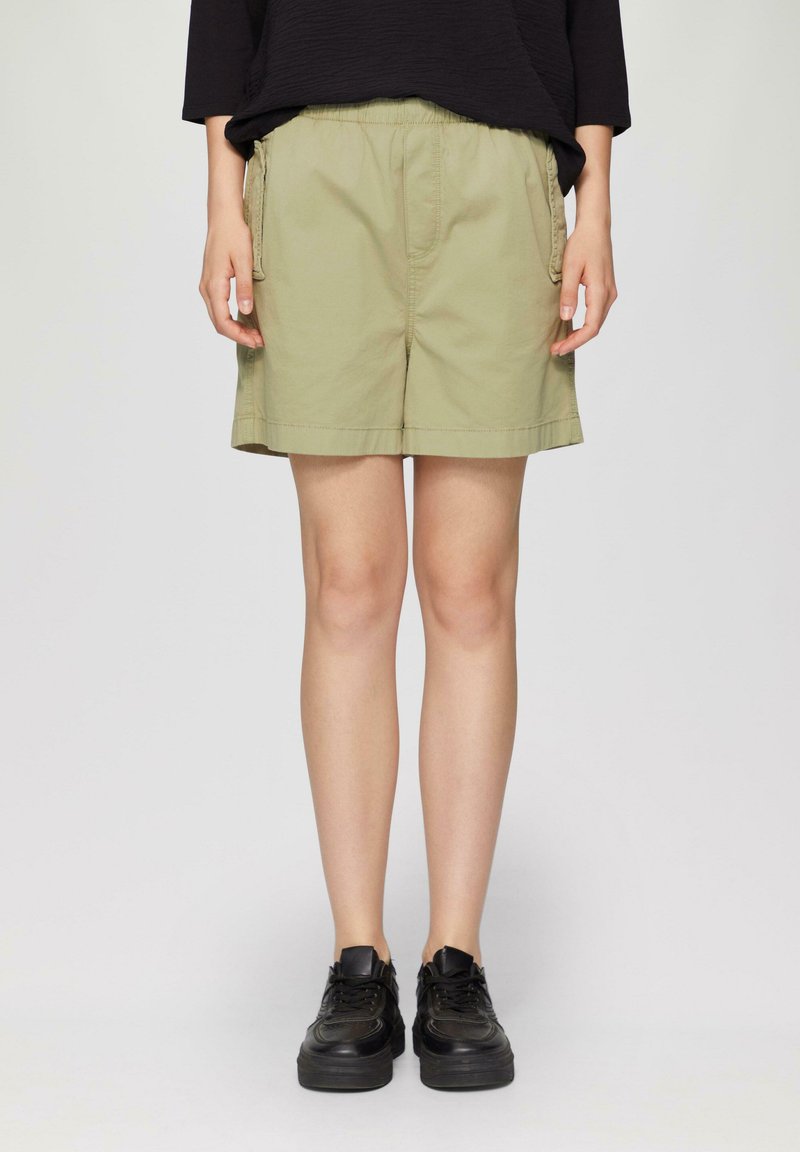 Khaki shorts met een elastische tailleband, zijzakken en een rechte snit, gecombineerd met zwarte sneakers. De stof lijkt zacht en duurzaam.