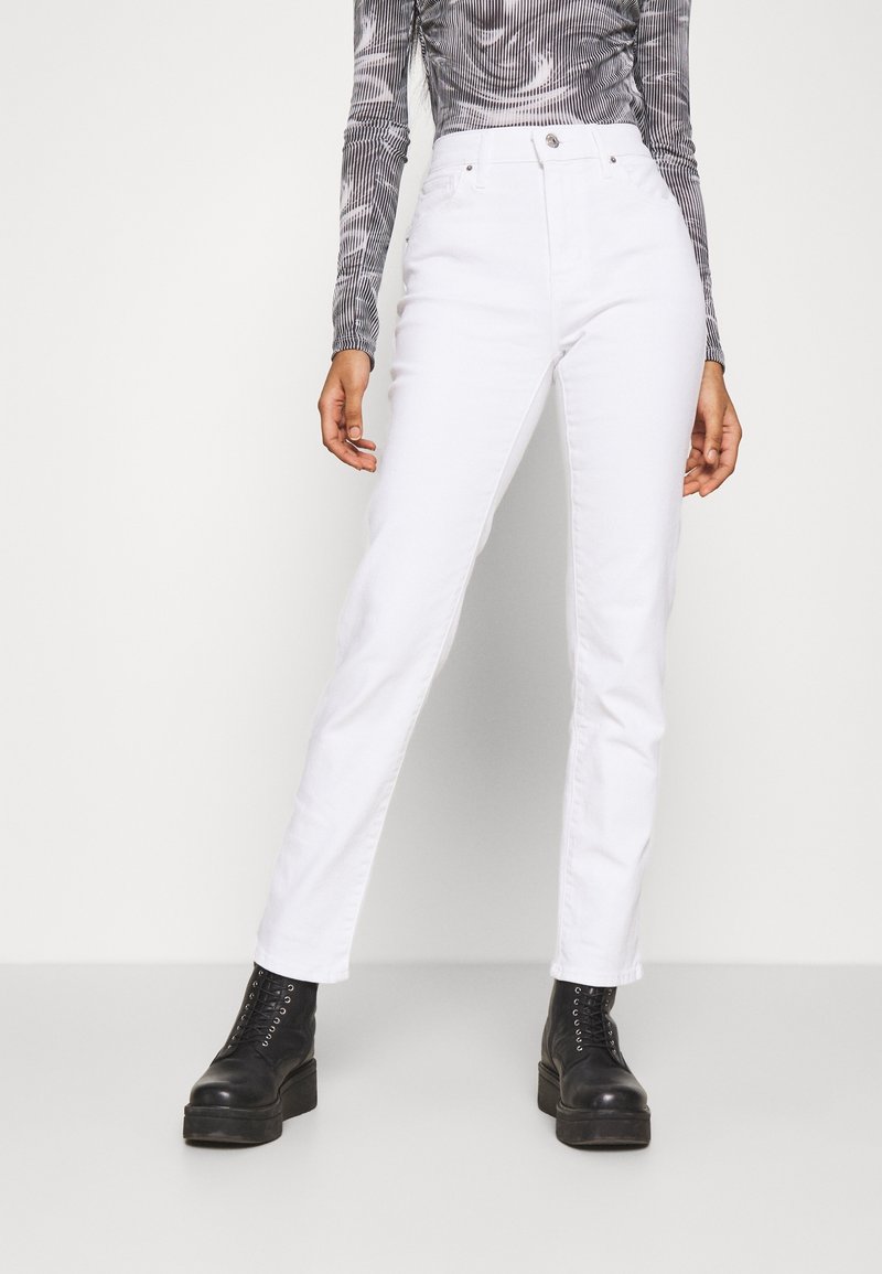 Pantalon en denim blanc à jambes droites avec une conception à cinq poches et une taille haute. Associé à des bottes noires à lacets et un haut à manches longues à motif.