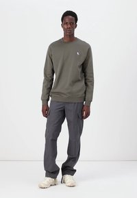 Olijfgroene sweatshirt met geribbelde halslijn en manchetten, gecombineerd met grijze cargobroek met meerdere zakken. Neutrale sneakers.